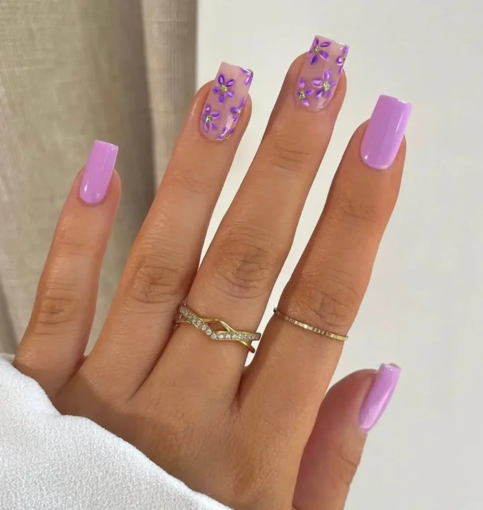 Square-shaped nails with a gilded lilac petals purple nail design, showcasing hand-painted purple flowers with tiny gold bead centers.
