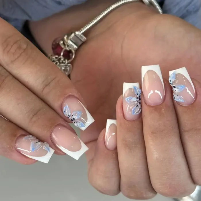 A modern French manicure with white tips, accented with a delicate, hand-painted blue and black flower.