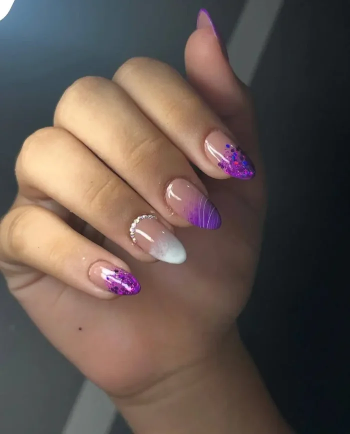 Almond nails with a cosmic amethyst sparkle purple nail design, featuring chunky purple glitter tips and artistic ombré.