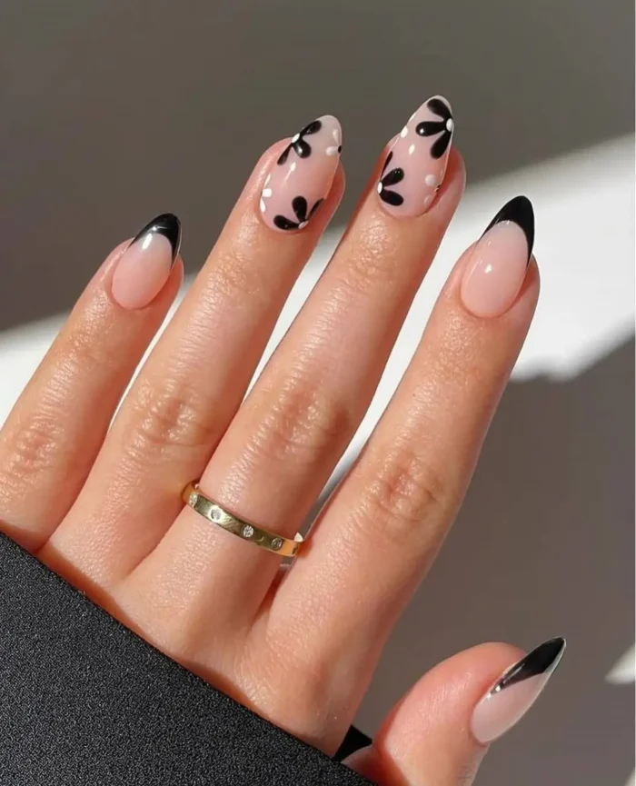 Almond-shaped nails with black French tips, accented by black abstract floral designs and white polka dots on a sheer nude base.
