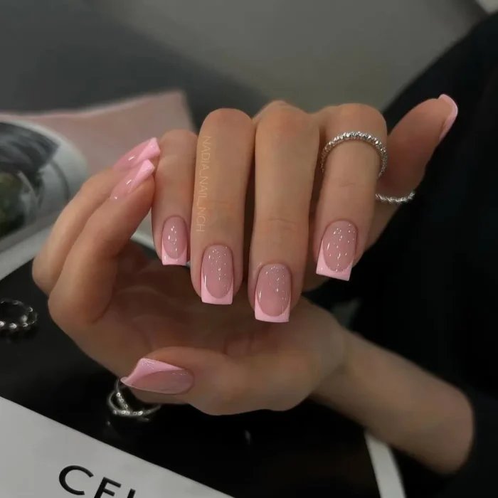 A hand with a chic French manicure on short square nails, featuring a sheer pink base and bright pink tips.