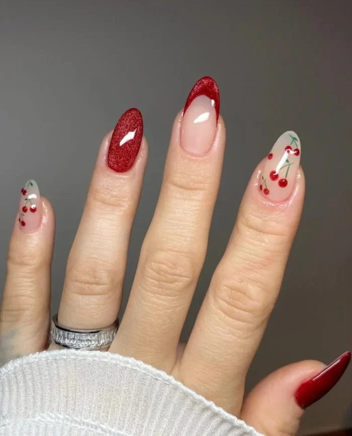 A playful mix-and-match red nail design featuring cherry nail art, a sparkling red glitter accent nail, and a red French tip.