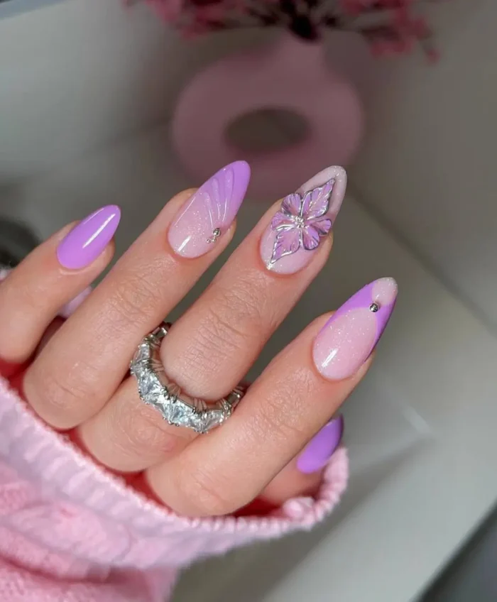 Nails with a lilac butterfly kiss purple nail design, featuring a 3D iridescent butterfly charm and chic color-blocking.