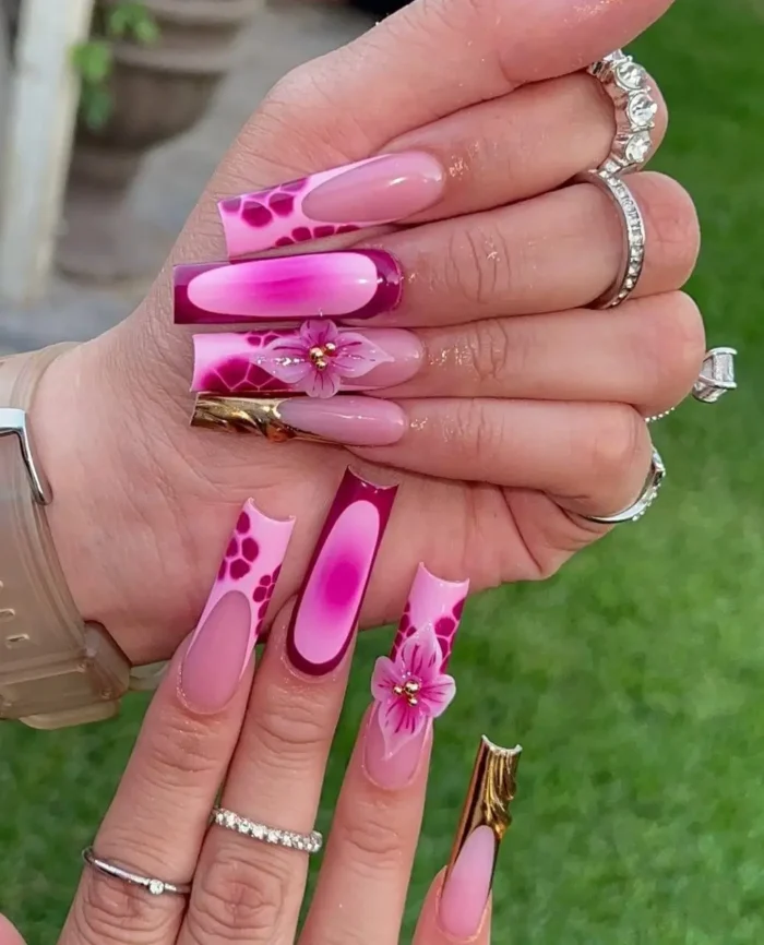 Long mixed-design nails in shades of pink featuring animal print, ombré, 3D flowers, and textured gold accents.