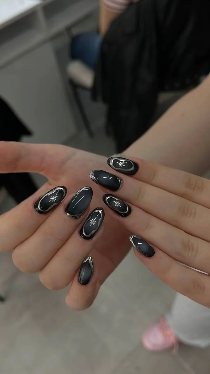Medium oval-shaped nails with a smoky dark gray base, adorned with silver starburst designs and fine silver outlines, resembling a night sky.