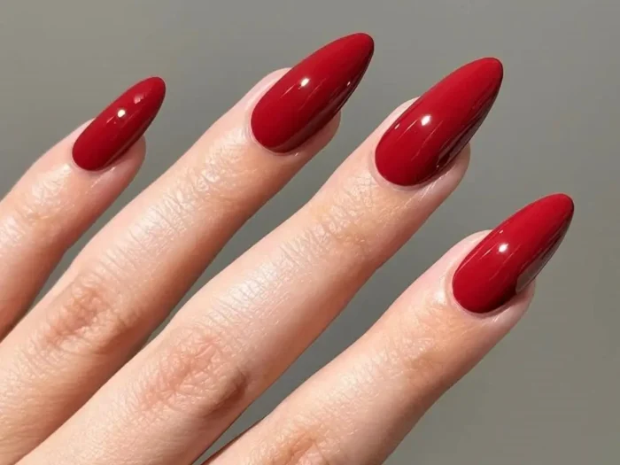 A flawless glossy red manicure on elegant, short almond-shaped nails, embodying a classic red nail design.