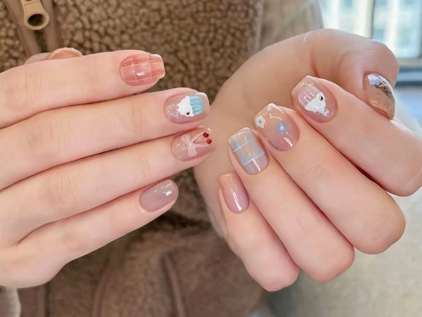 Hands showing cute short nail designs featuring a mix of plaid patterns and character illustrations on a sheer base.