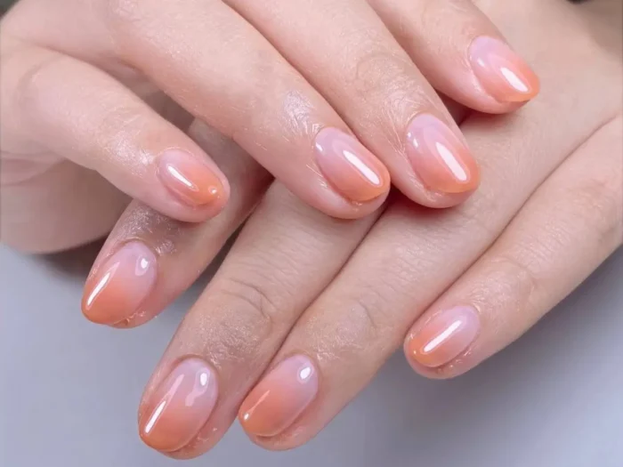 Close-up of cute simple gel nails featuring a soft peach and pink ombre effect on short rounded nails, an idea for an easy, chic manicure.