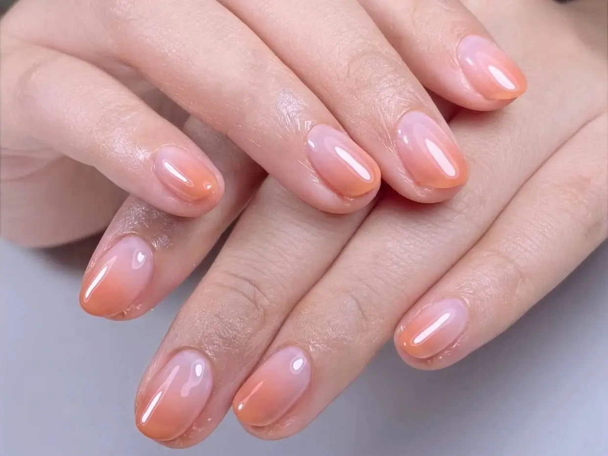 Close-up of cute simple gel nails featuring a soft peach and pink ombre effect on short rounded nails, an idea for an easy, chic manicure.