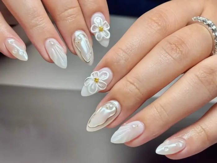 Elegant white nail designs featuring pearlescent finishes and 3D floral art.