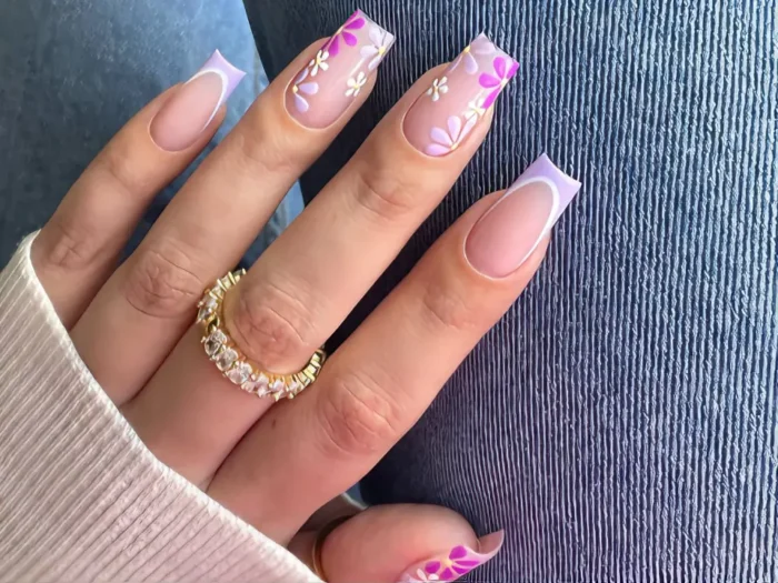 A unique spring nail design on long square nails, featuring a modern lilac purple French manicure combined with abstract white and pink floral accent nails.