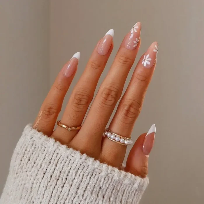A cute white nail design on long almond nails, featuring a French manicure with a white daisy accent nail.