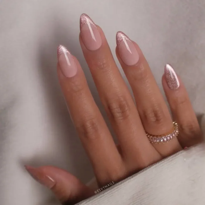 A close-up of a hand with a modern French manicure featuring shimmering pink cat eye tips and a matching accent nail on an almond nail shape.
