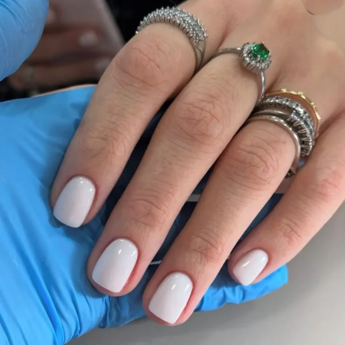 A hand adorned with silver rings, showcasing a crisp, opaque white manicure on short, squoval-shaped nails.