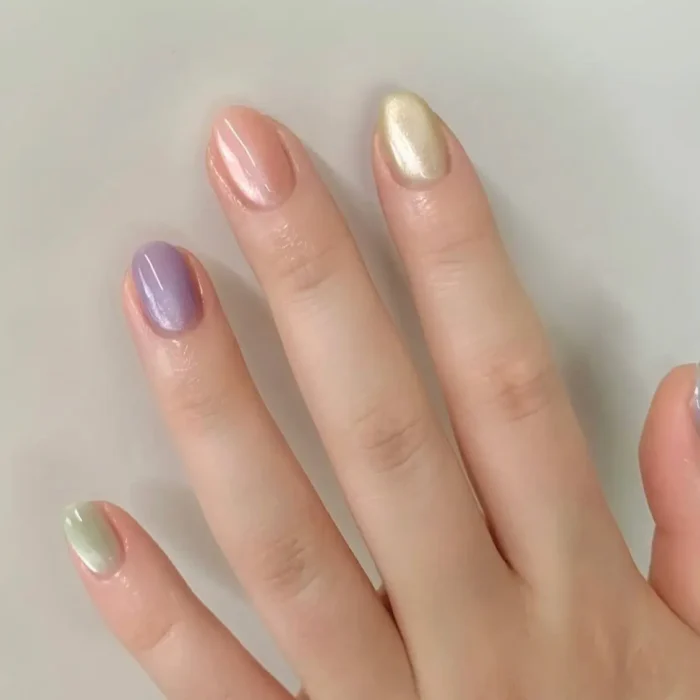 Short nails painted with a glossy, iridescent pastel gel polish in shades of mint green, lavender, peach, and pale yellow.