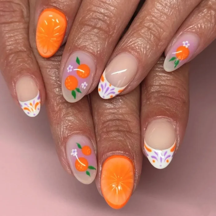 A close-up of a themed fruit nail design featuring clementine slices and a decorative orange and purple folk art pattern on the tips.