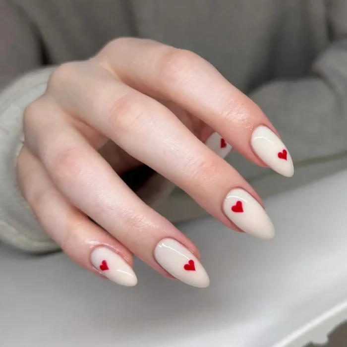 A cute white nail design on almond nails, featuring a milky white base with a single small red heart accent on each nail.