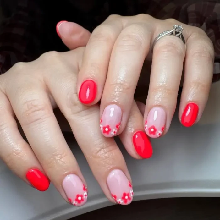 Short nails featuring a mix of solid vibrant red gel polish and sheer nude nails with red and white floral French tips.