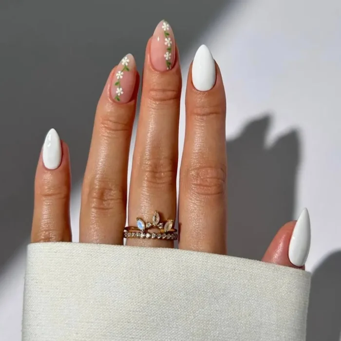A cute white nail design on almond nails, mixing solid white polish with a floral vine accent nail.