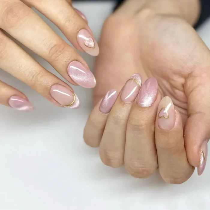 A sophisticated pink cat eye manicure on almond nails, featuring gold line art of hearts and butterflies on sheer accent nails.