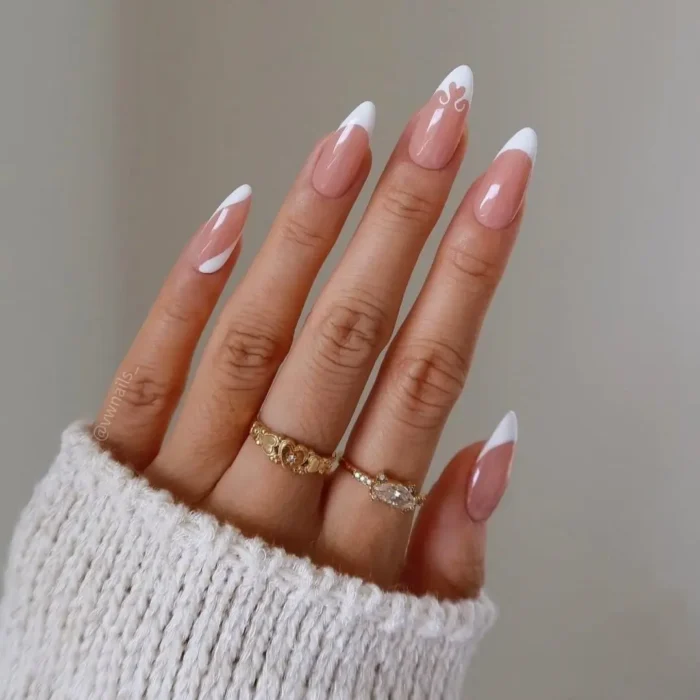 A cute white nail design on almond nails featuring a mix of classic French tips, abstract waves, and a heart accent.