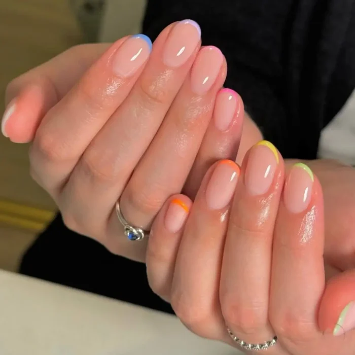 Short, oval-shaped nails with a clear base and thin, colorful French tips in various bright shades like blue, pink, orange, yellow, and green.
