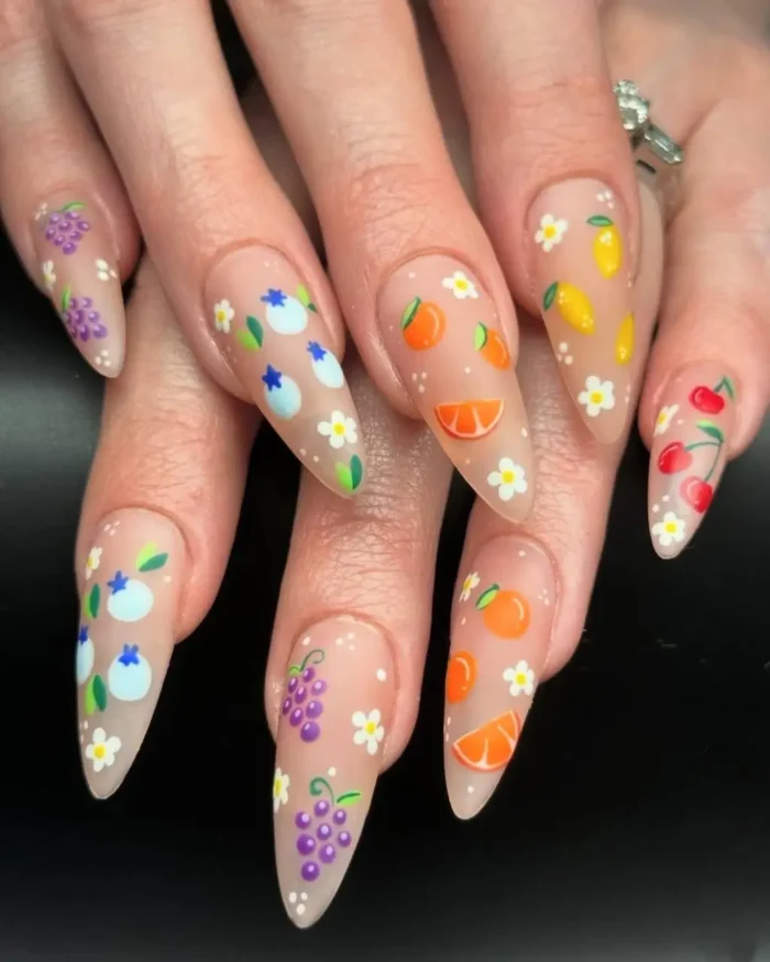 A hand with long stiletto nails showing a delicate mixed fruit and flower design on a matte base.