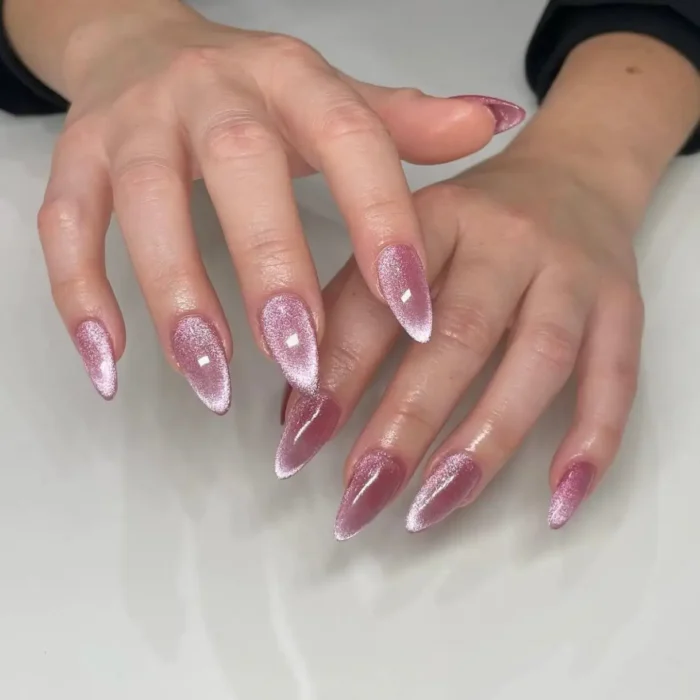 A sophisticated pink cat eye manicure on long almond nails, featuring a sharp, angled shimmer effect.