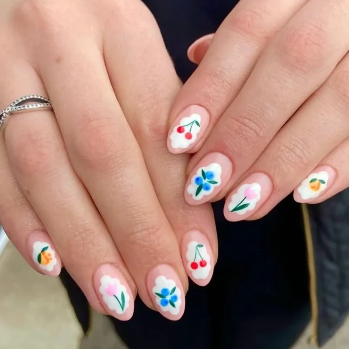 Close-up of a delicate fruit and flower nail design, with each motif painted inside a white framed cameo on almond nails.