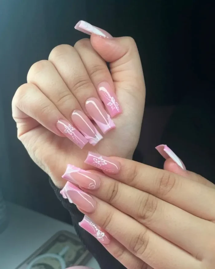Long square pink nails with abstract blush and white tips and delicate floral line art.