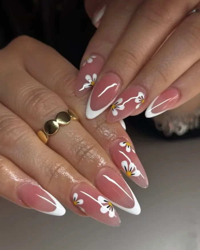 A cute white nail design on long almond nails featuring a French manicure with a trailing daisy vine accent.