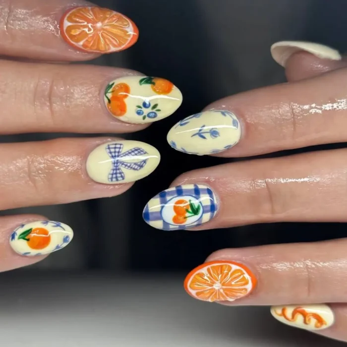 A close-up of a fruit nail design inspired by hand-painted pottery, with oranges and blue gingham on a cream base.