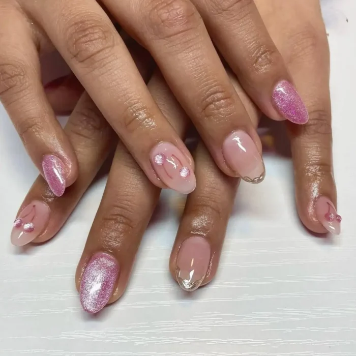 A playful manicure mixing glittery pink cat eye nails with sheer accent nails adorned with tiny 3D cherry charms.