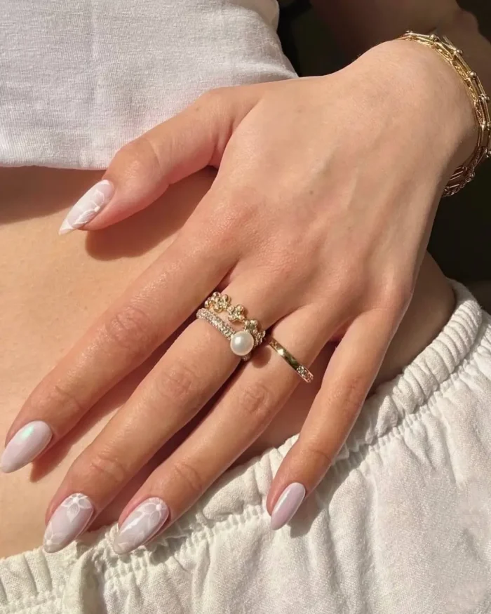 An elegant white nail design featuring a pearlescent base with intricate white lace floral patterns on accent nails.
