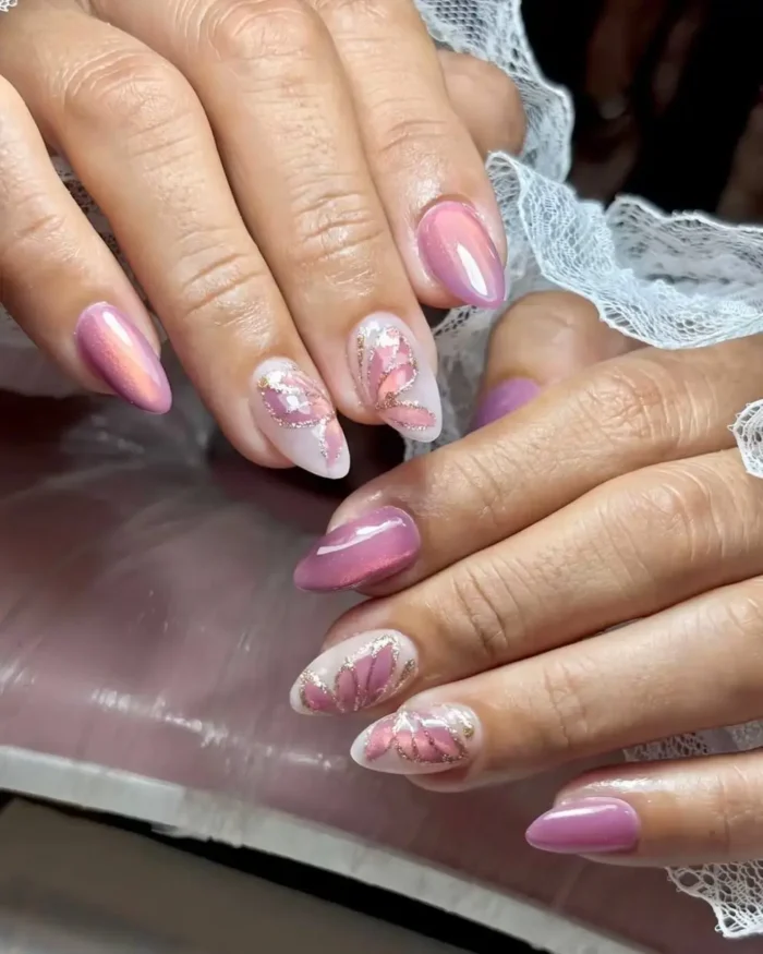 A romantic pink cat eye manicure on almond nails, featuring accent nails with abstract butterfly wing art and gold glitter details.