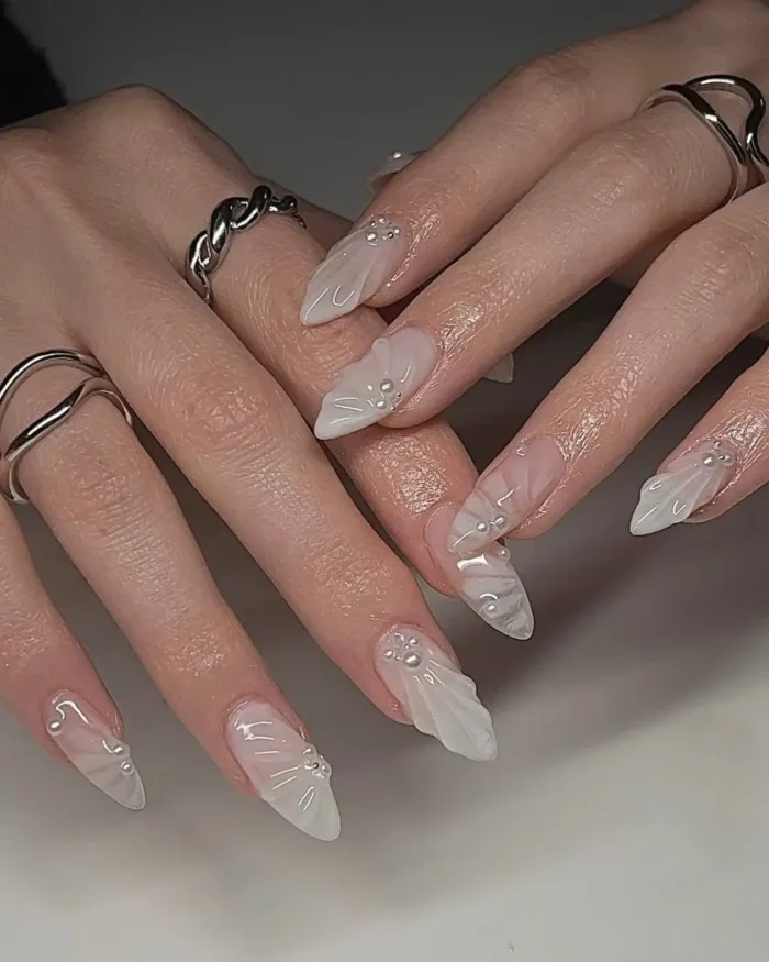 An elegant white nail design on long stiletto nails with a 3D sculpted seashell texture and pearl accents.