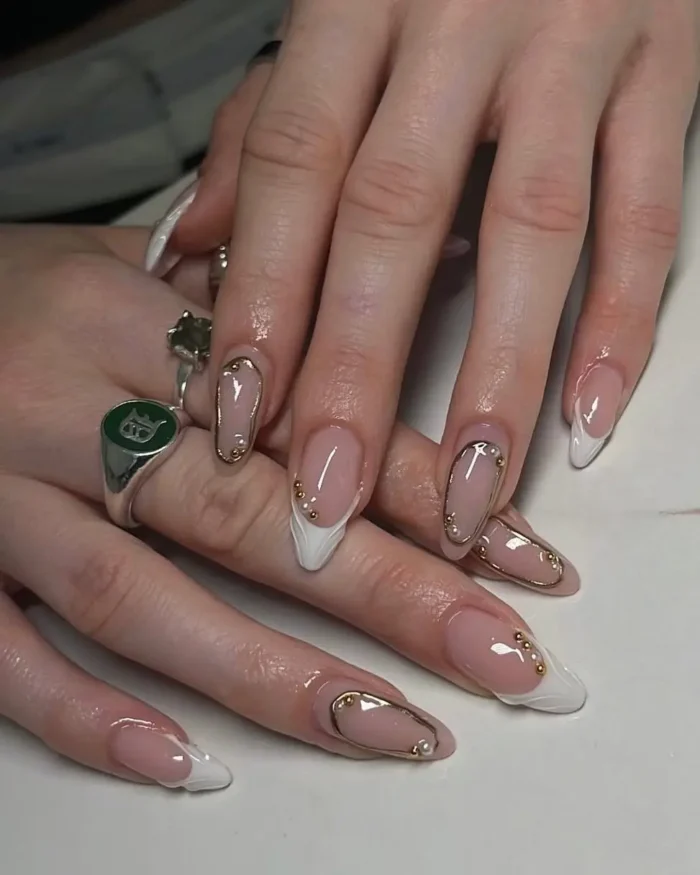 An elegant white nail design on long nails, featuring a mix of deep white French tips and gold-framed accents with pearl details.