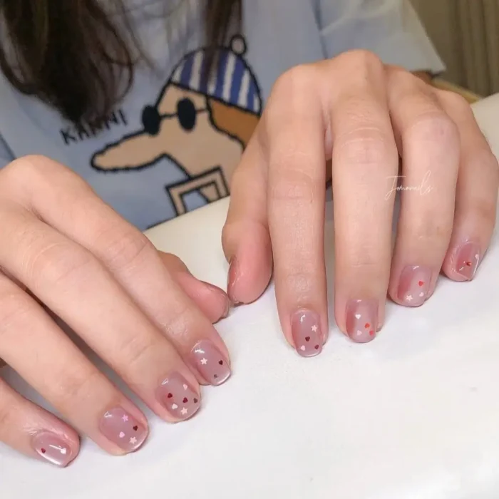 Short, natural-toned nails with a scattering of small red hearts and shimmering silver stars.