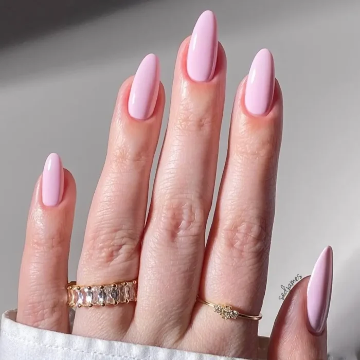 A beautiful close-up of long, almond-shaped nails with a glossy, classic bubblegum pink manicure.