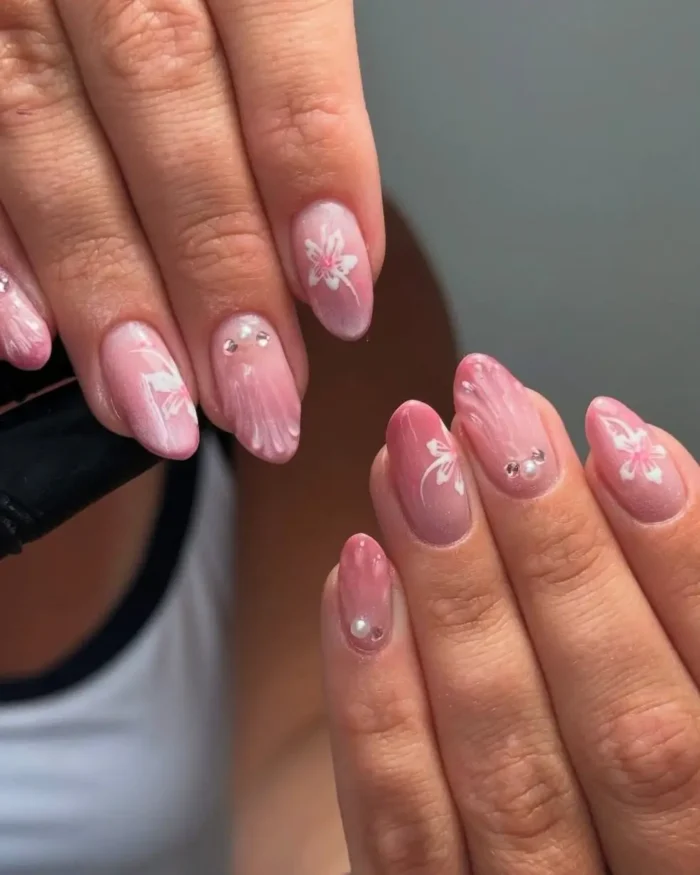 An artistic pink cat eye manicure on oval nails, featuring abstract white floral art and delicate pearl embellishments.