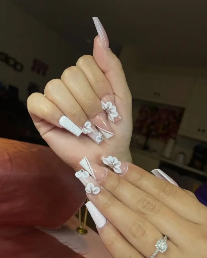 An elegant white nail design on long coffin nails, featuring 3D flowers, a sugar glitter texture, and geometric lines.