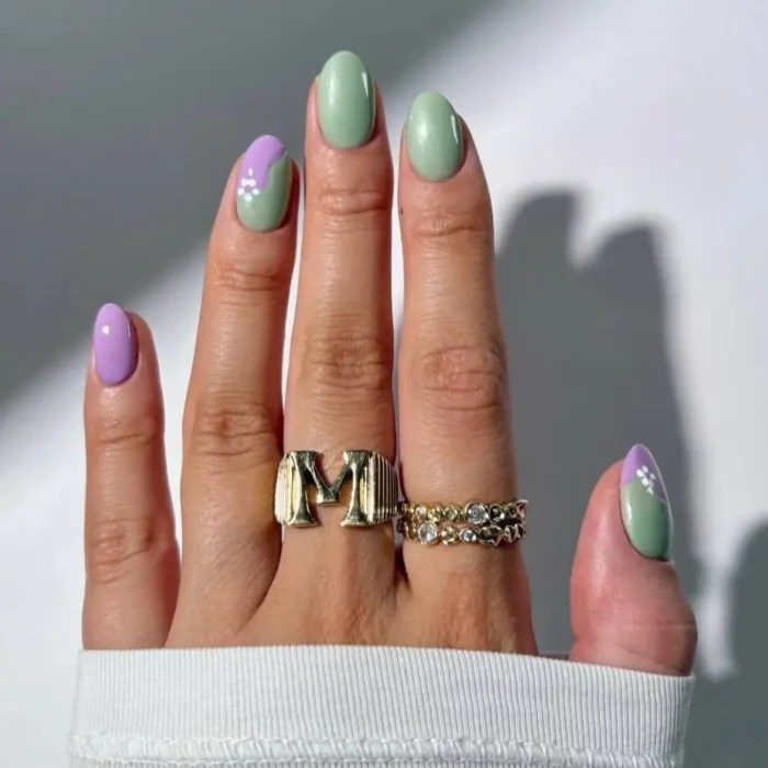 Short, oval nails with a two-toned gel design, featuring lavender and mint green in a half-moon pattern, accented by small white dots.