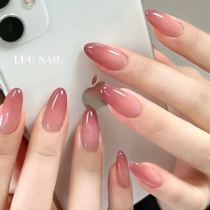 Hands holding a white phone, showcasing a rosy jelly ombre manicure on glossy, almond-shaped nails.