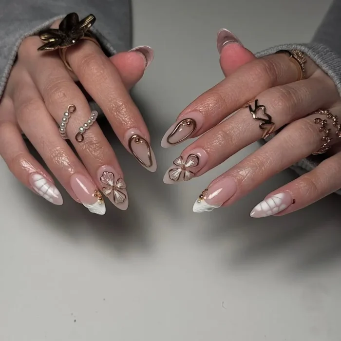 An elegant white nail design on almond nails featuring a mix of abstract tips, gold-outlined florals, and framed accents.