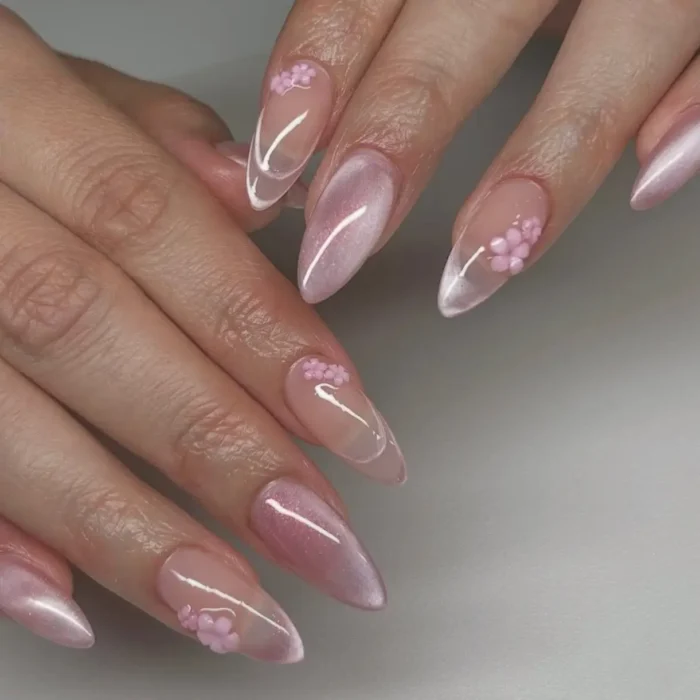 An intricate manicure on long stiletto nails, mixing pink cat eye designs with sheer nails featuring 3D pink flowers and white swirls.
