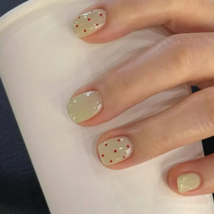 Short, oval nails painted in a light pastel green gel, with some nails featuring small, evenly spaced red polka dots.