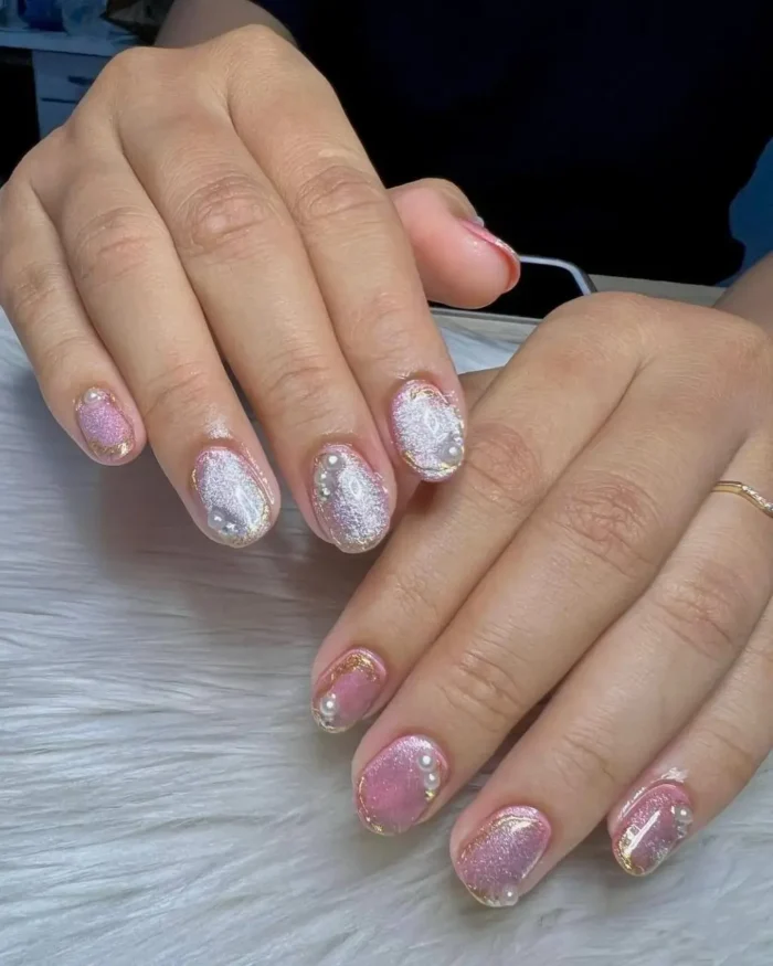A detailed manicure on short nails featuring a mix of pink and silver cat eye polish, with delicate gold outlines and pearl embellishments.