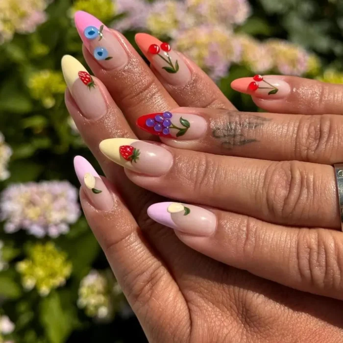 A modern fruit nail design on long stiletto nails, featuring 3D fruit art over colorful pastel French tips.