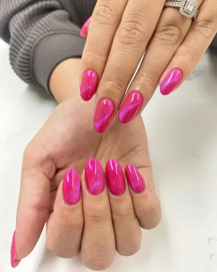A vibrant fuchsia pink cat eye manicure on oval-shaped nails, showcasing a bright and energetic shimmer.