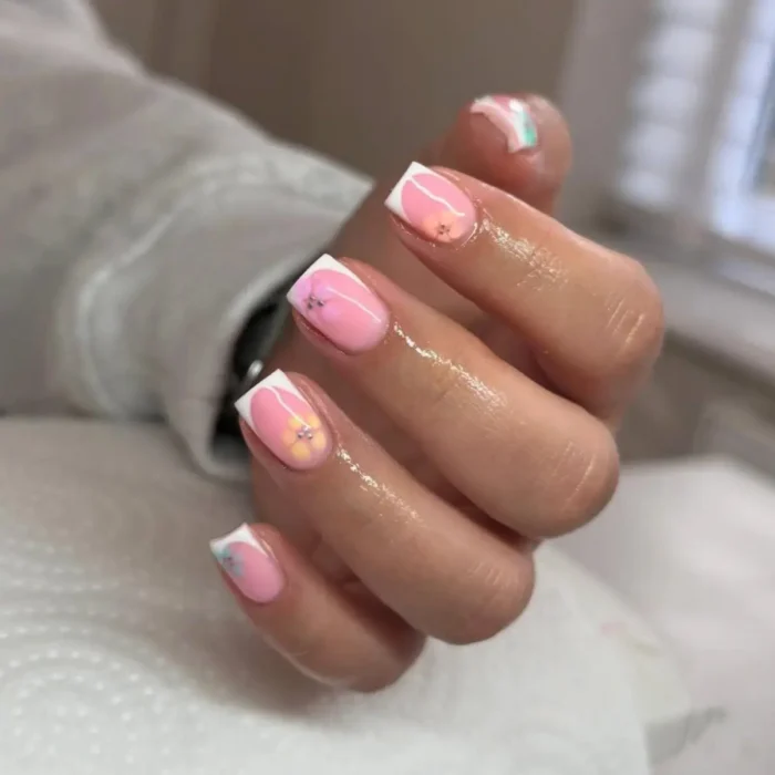 Short, squared-off nails with a pink gel base and white French tips, adorned with small yellow and pink flower decals.
